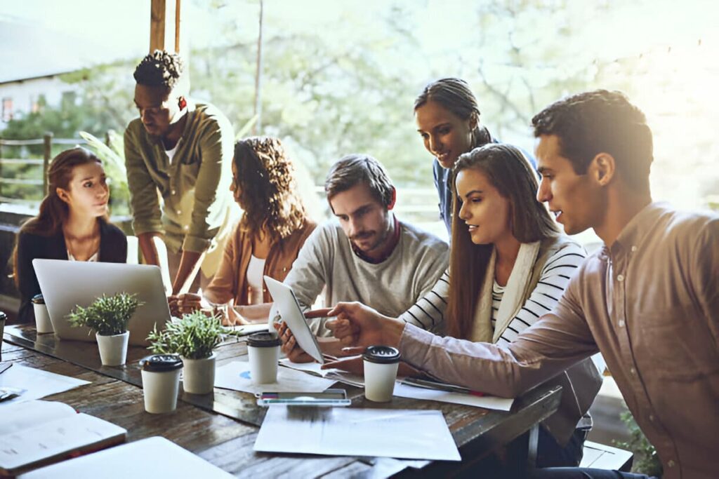 A diverse group of individuals sitting around a table, engrossed in their work on laptops.