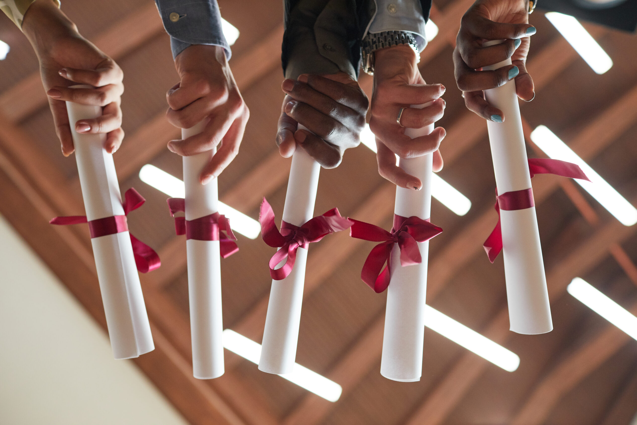 Low angle closeup of young people holding diplomas with red ribbon during graduation ceremony in college, copy space